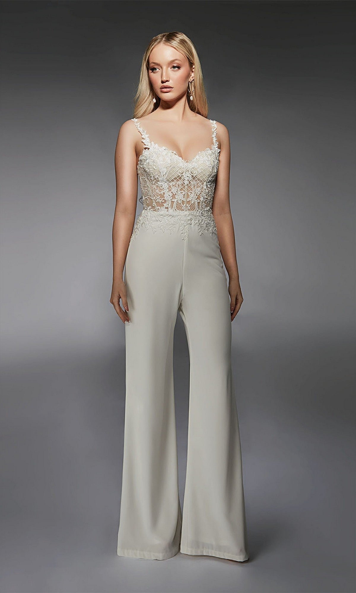 A woman poses in the Long Formal Jumpsuit: Alyce 70074, featuring a sheer lace bodice with floral embroidery, spaghetti straps, and wide-leg pants against a plain gray background.